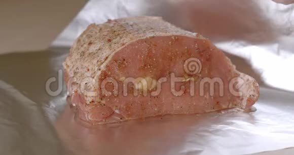 男性厨师用食物箔包裹一块新鲜的猪肉腌制后撒上香料然后塞上大蒜准备制视频的预览图