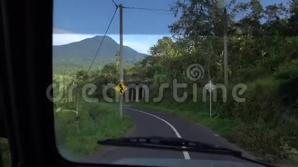 一条弯曲的道路从前面的汽车驾驶道路在巴厘岛印度尼西亚沿着树状的道路和视频的预览图