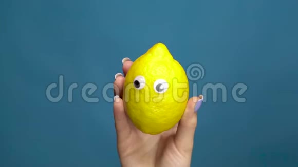 柠檬的眼睛在一个女人的手特写柠檬在蓝色背景上摇动和扭曲眼睛慢动作视频的预览图