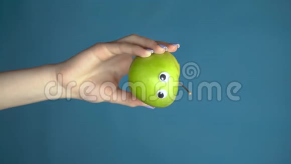 绿色的苹果眼睛在一个女人的手闭上苹果在蓝色背景下环顾四周垂直视频视频的预览图