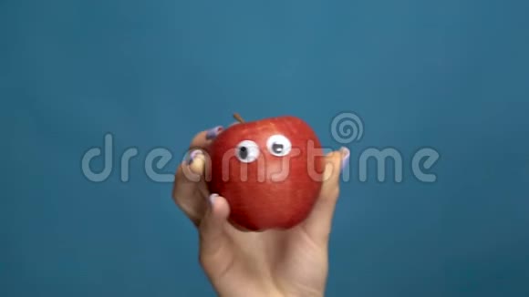 红苹果的眼睛在一个女人的手特写苹果在蓝色背景上摇动和扭曲眼睛慢动作视频的预览图