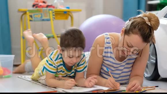 年轻快乐的母亲和小儿子躺在孩子们房间里一起做工艺品画画视频的预览图