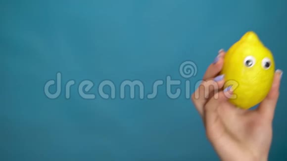 女人手里拿着眼睛的柠檬柠檬跳进框架在蓝色背景上环顾四周女人的手特写视频的预览图