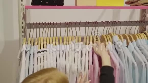 女性手触摸衣架与衬衫在服装陈列室卖方在时装精品店布置衣架视频的预览图