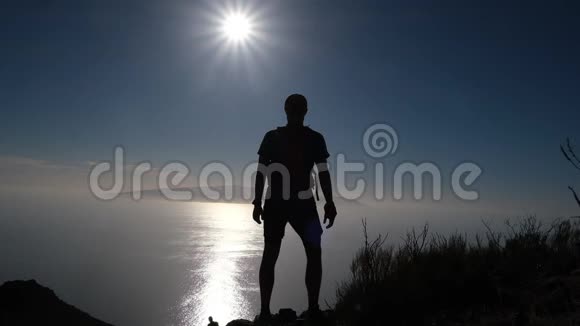 站在山顶上的一个快乐徒步旅行者的剪影慢动作视频的预览图