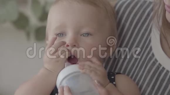 一个漂亮的女婴在厨房里和妈妈的帮助下从小婴儿瓶里喝水一种概念视频的预览图