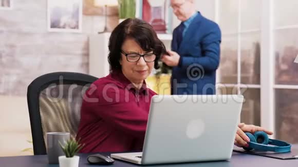 在笔记本电脑上工作的老妇人一边喝咖啡视频的预览图