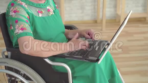 靠近一位老年妇女她的手在笔记本电脑上打字坐在轮椅上视频的预览图