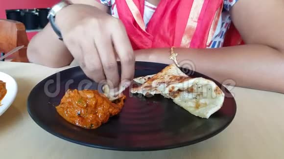 双手撕着黄油Naan一边吃着餐厅里黑色盘子里的鸡肉提卡黄油masala肉汁视频的预览图