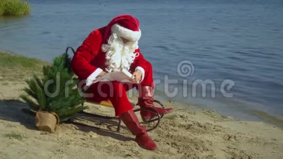 圣诞老人坐在湖沙岸上的雪橇上在纸上写下一些东西海上的圣诞老人视频的预览图