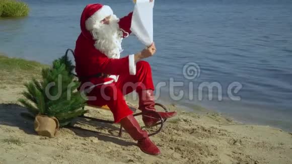 圣诞老人坐在沙滩上的雪橇上从一张纸上读到一些东西视频的预览图