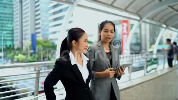 两个年轻的工作妇女在现代桥上愉快地讨论视频的预览图