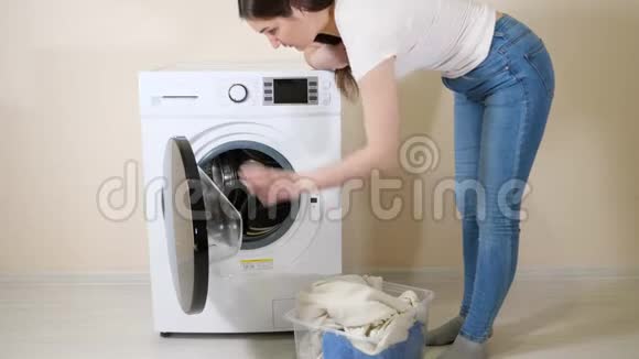 女人把脏衣服装在米色墙附近的洗衣机里视频的预览图
