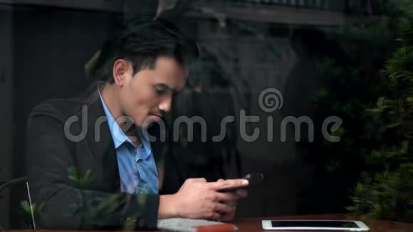 年轻的商人在玻璃窗附近使用智能手机视频的预览图