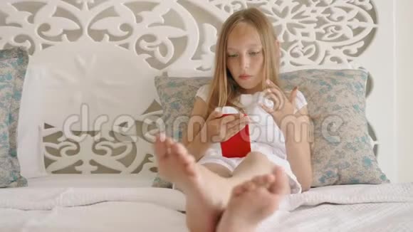 可爱的少女长发躺在床上使用红色智能手机视频的预览图