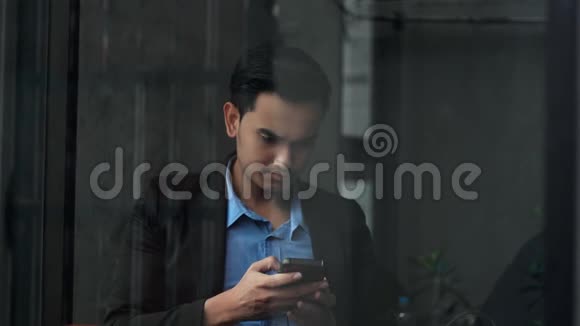 英俊的商人在玻璃窗户附近有智能手机问题视频的预览图