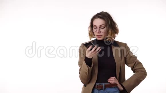 穿着时尚休闲服装的漂亮黑发女人在她的手机上记录了一条声音信息白色背景下视频的预览图