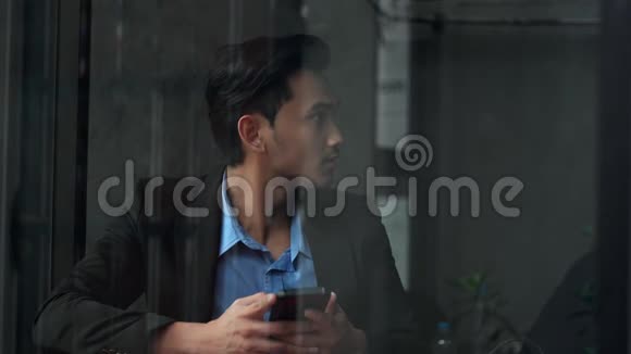 这位英俊的商人在玻璃窗附近使用智能手机视频的预览图