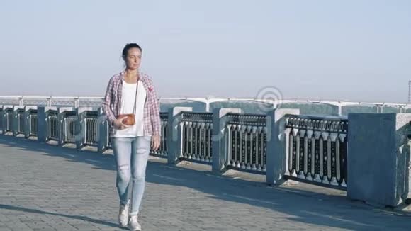 慢动作美丽的女人沿着海滨漫步用复古相机和看河视频的预览图