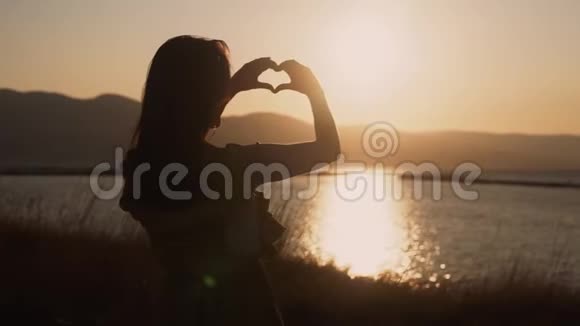 女人的双手以海洋和日落为背景缓慢的动作塑造心形视频的预览图