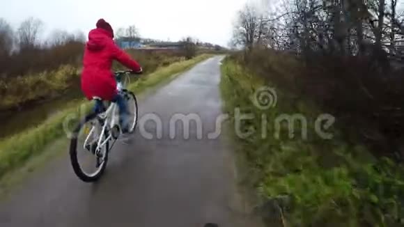 一个穿红色夹克的女孩骑着白色自行车在柏油路上视频的预览图