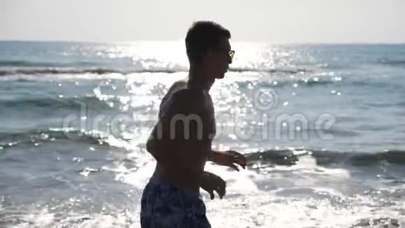 运动帅哥早上沿着海边慢跑年轻的运动男子跑过海边接近男性视频的预览图