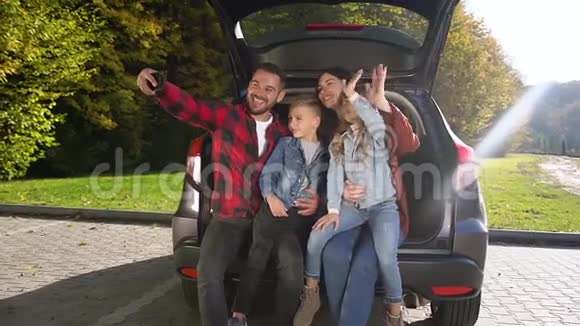 一幅迷人的家庭肖像坐在后备箱里挥舞着双手在视频的预览图