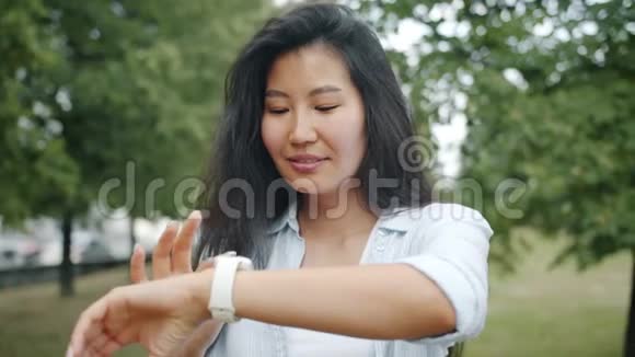 夏天在城市公园使用智能手表触摸屏幕的快乐亚洲女孩视频的预览图