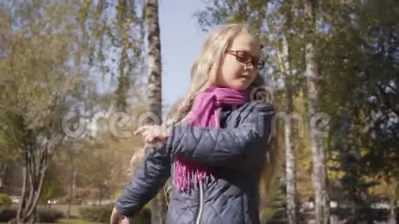 白人少女金发碧眼在秋天的公园或森林里的树木间旋转视频的预览图