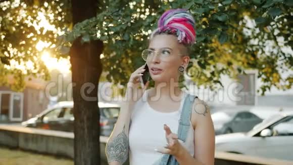 有纹身和五颜六色头发的女孩在城市公园用手机说话视频的预览图