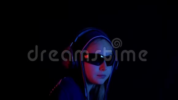 少女戴着头巾和黑色太阳镜听着耳机音乐在黑暗的房间里红色和蓝色的灯光肖像视频的预览图