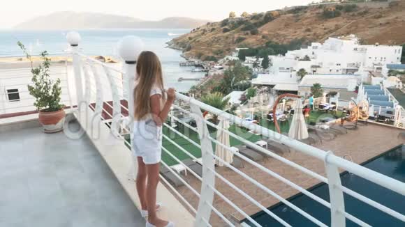 穿着白色衣服的少女站在海上的户外露台和游泳池景观上度假胜地的旅游女孩视频的预览图