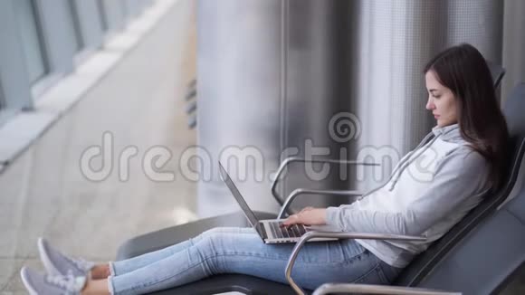 年轻女子坐在候机室用笔记本电脑在机场工作视频的预览图