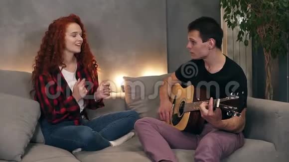 一位丈夫正在为他的妻子唱一首歌弹一把吉他妻子也和他一起坐在沙发上唱歌视频的预览图