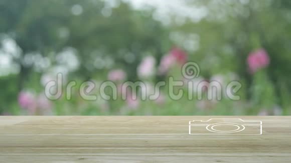 木制桌子上的相机平面图标在花园中模糊的粉红色花朵和树上商业相机服务商店的概念视频的预览图
