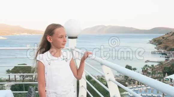 十几岁的女孩走在户外露台上有海和山的景观夏日阳台上的幸福女孩抚摸扶手视频的预览图