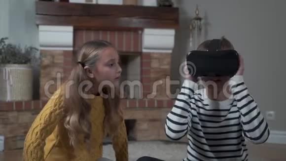 可爱的白种人男孩戴着VR眼镜和漂亮的女孩说话环顾四周哥哥和姐姐一起玩视频的预览图