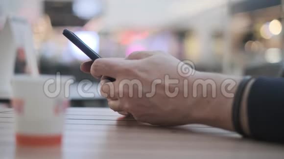 一个年轻人坐在购物中心的咖啡厅里用智能手机的手视频的预览图