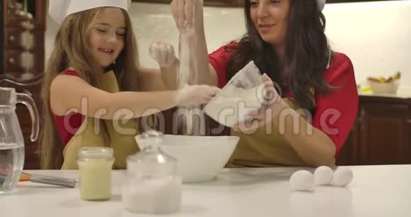 白人母女从盘子里倒出面粉小女孩帮她妈妈做饭快乐的微笑视频的预览图