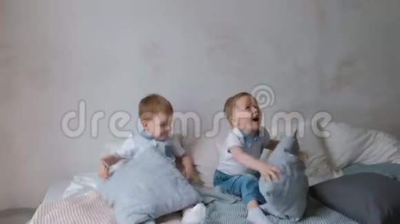 双胞胎男孩蹒跚学步的孩子躺在床上扔枕头跳跃和大笑视频的预览图
