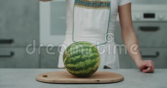 职业厨师女士用一把大刀切了一个大西瓜在厨房前的镜头肖像捕捉视频的预览图