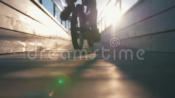小男孩的剪影骑着一辆自行车在日落时分的木桥上经过一位女小提琴手视频的预览图