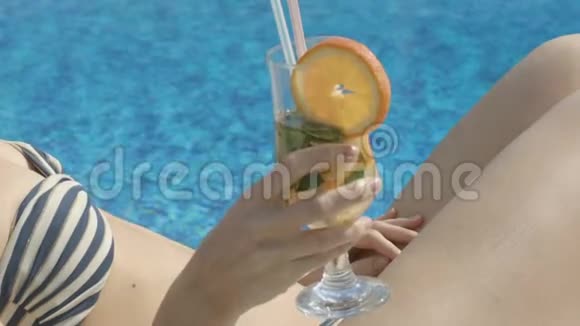 苗条的女士在宽敞的游泳池旁喝着清爽的鸡尾酒沐浴阳光视频的预览图