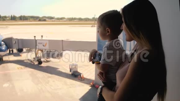 在国际机场航站楼跑道上母亲带着蹒跚学步的儿子观看喷气式飞机的4k镜头视频的预览图