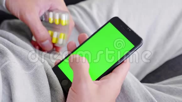 男人坐在沙发上用智能手机安装绿色的模拟屏幕然后吃药视频的预览图
