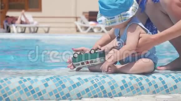 小男孩玩玩具巴士和妈妈坐在游泳池里暑假视频的预览图