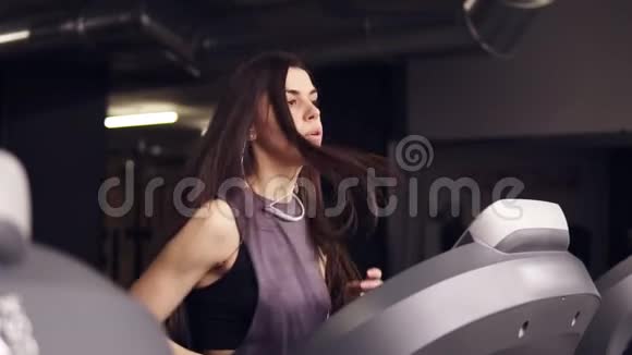 漂亮的黑发女孩留着长发穿着干燥的运动服在跑步机上跑步视频的预览图
