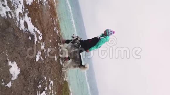 冬天年轻美丽的女性和西伯利亚哈士奇狗在海滩上散步动作缓慢视频的预览图