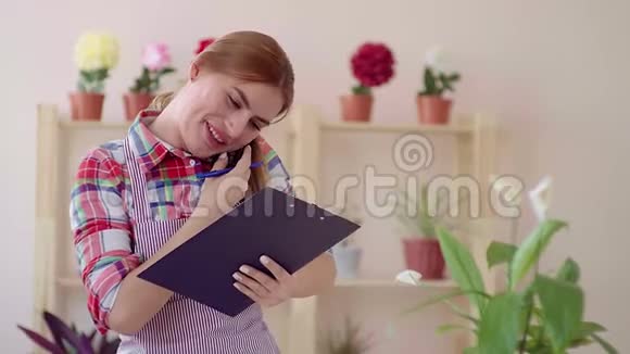 小生意开一家花店一个女孩穿着格子衬衫和一条条纹围裙手里拿着一张纸微笑着视频的预览图