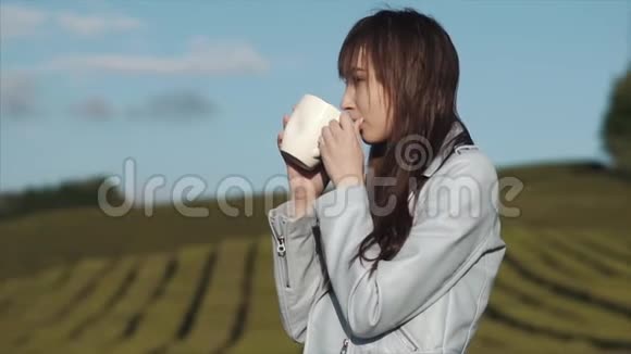 一个迷人的女人正站在茶园里喝着一大杯白茶视频的预览图